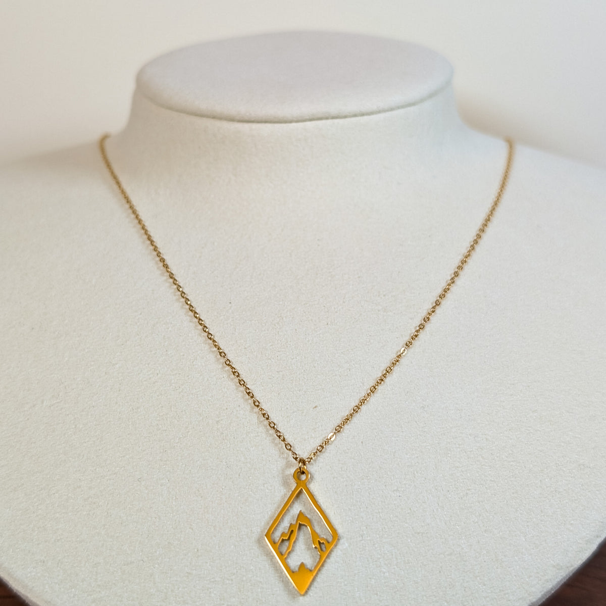 Gold-tone stainless steel necklace with a cut-out mountain range in a diamond frame on a white display bust