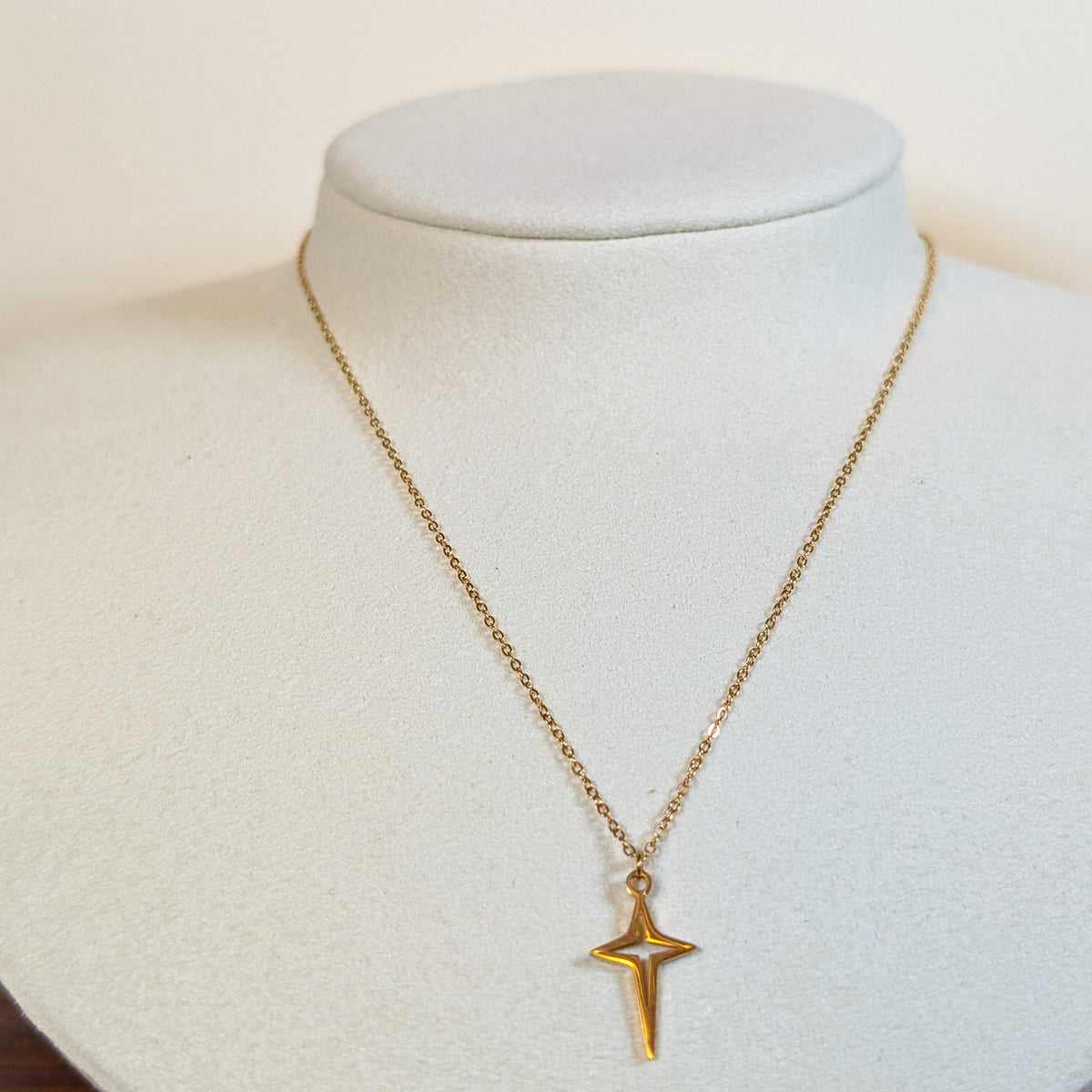 Gold-tone stainless steel necklace with an elongated four-point north star pendant on a white display bust