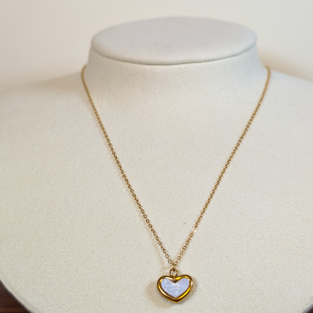 Gold-tone stainless steel necklace with a pale blue opal heart pendant on a white display bust