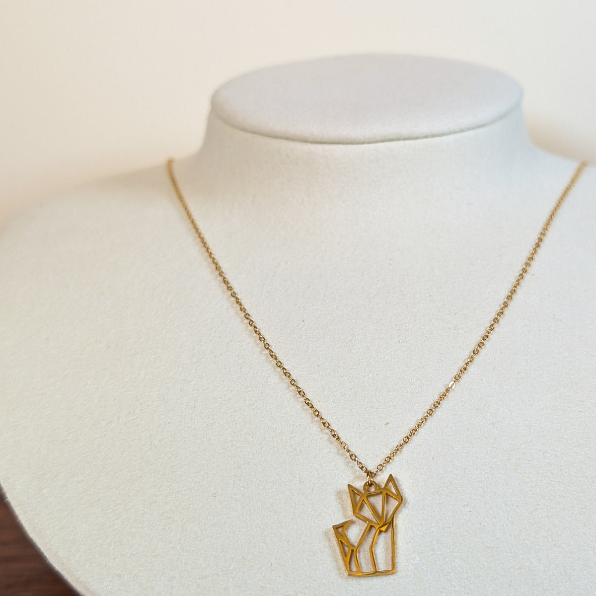 Gold-tone stainless steel necklace with a cut-out origami cat pendant on a white display bust