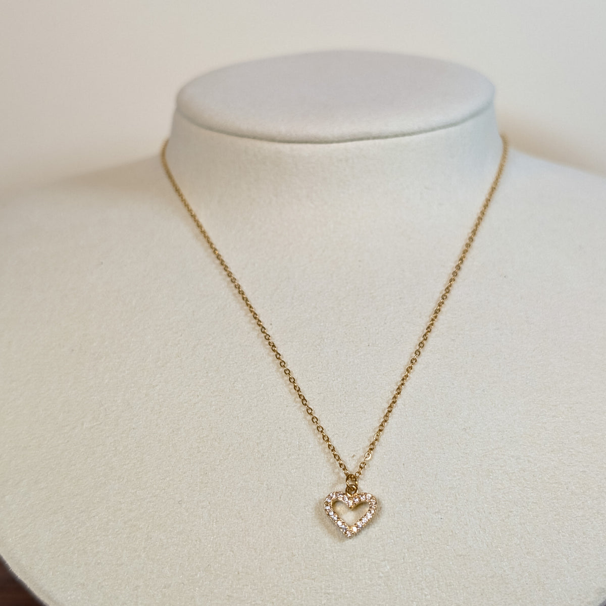 Gold-tone stainless steel necklace with a pave-set open heart pendant on a white display bust