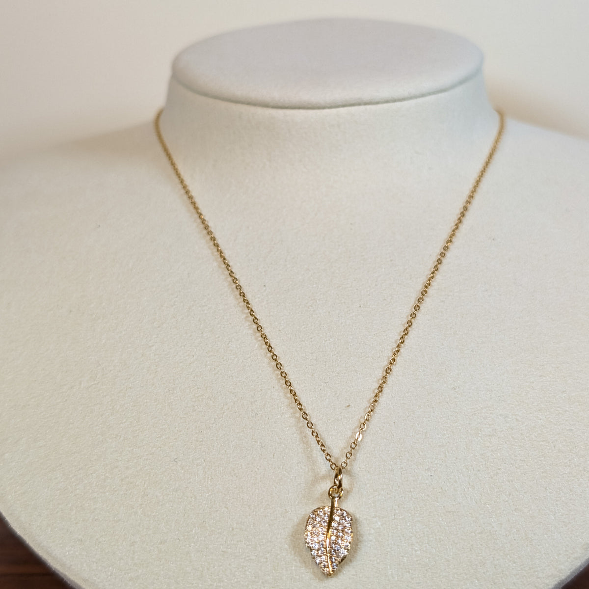 Gold-tone stainless steel necklace with a pave-set leaf pendant on a white display bust