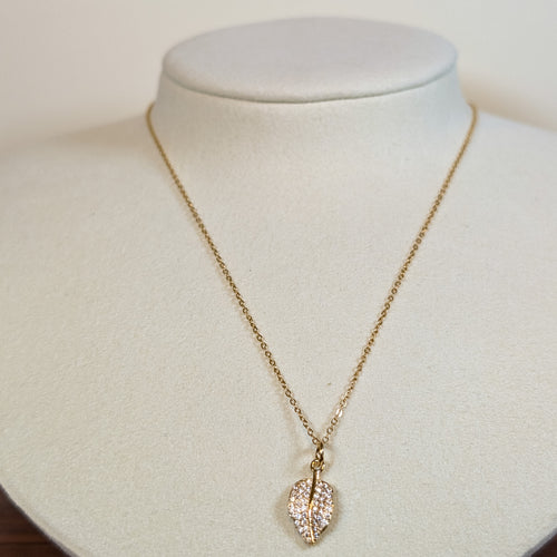 Gold-tone stainless steel necklace with a pave-set leaf pendant on a white display bust