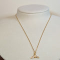 Gold-tone stainless steel necklace with a stone-set whale tail pendant on a white display bust