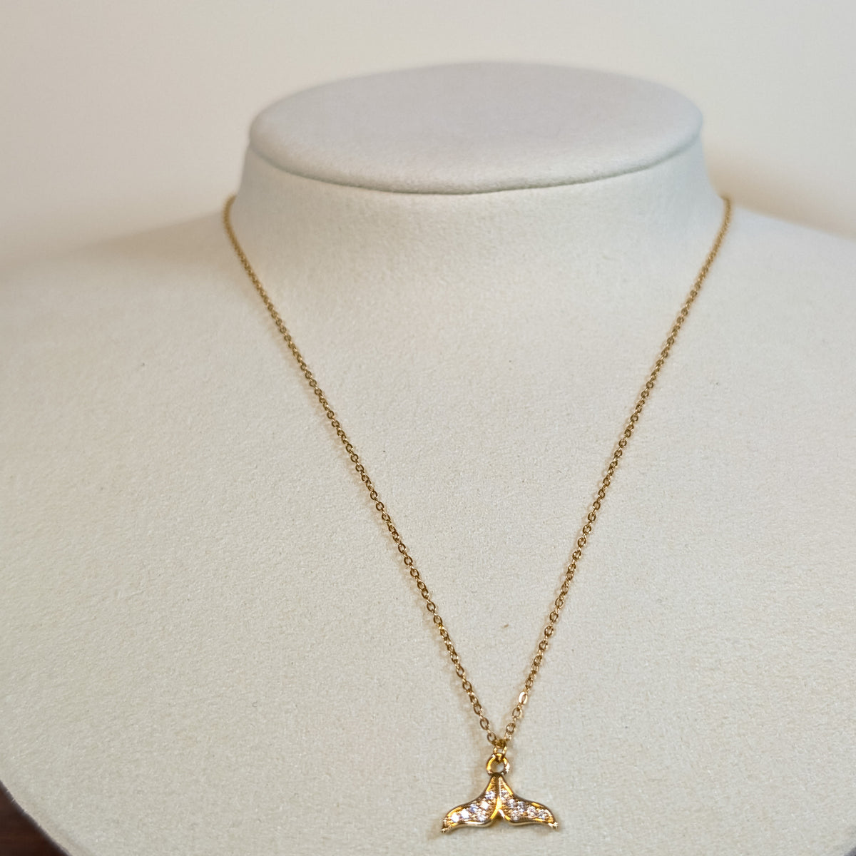 Gold-tone stainless steel necklace with a stone-set whale tail pendant on a white display bust